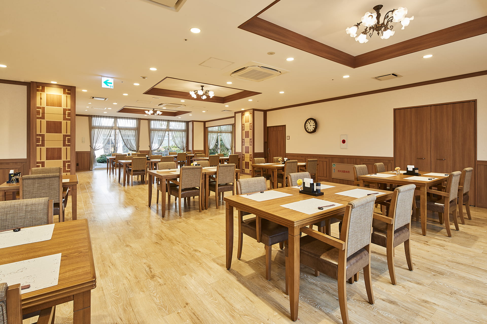 木材と照明を基調とした広々とした食堂。複数のテーブルと椅子が配置された明るい空間。